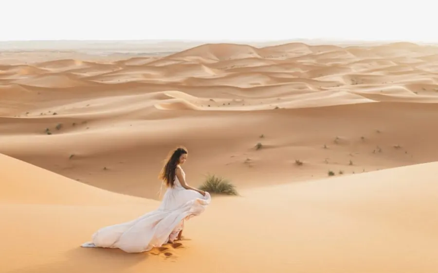 A woman in a white dress sitting on a Sahara dune