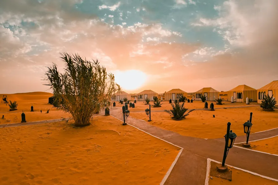 A desert camp at sunset, with lanterns lining the path between the tents