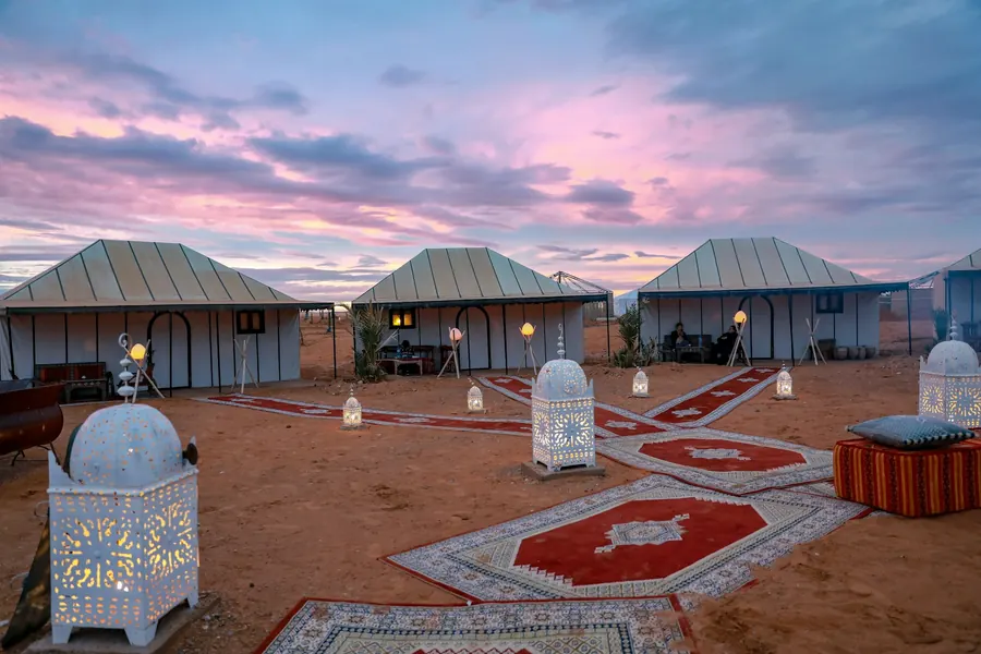 Desert camp tents with lanterns and carpets at dusk