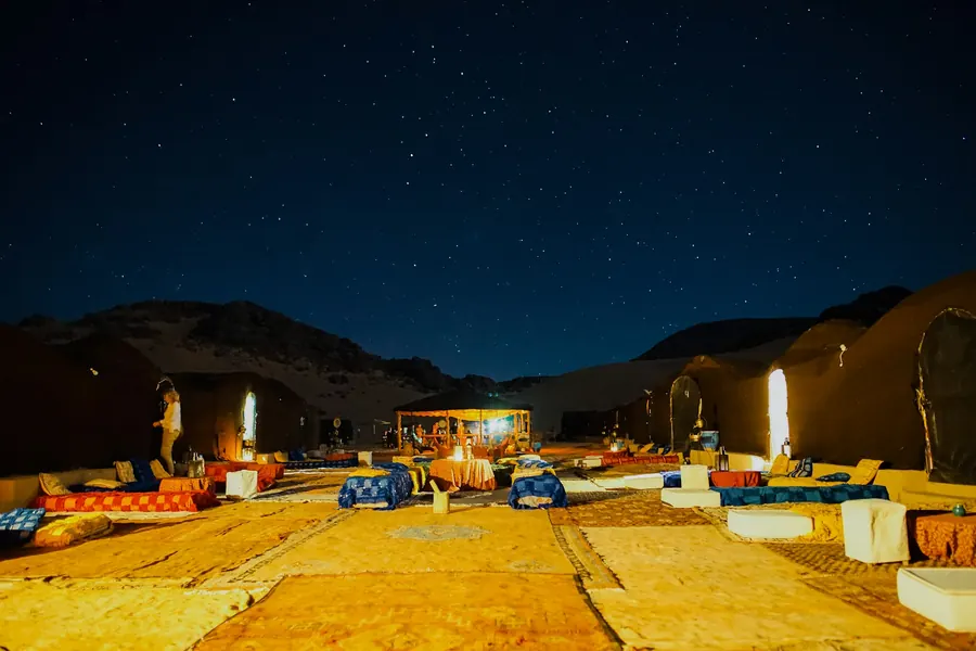 Cushions, carpets and lanterns laid out in a desert camp under a starry sky