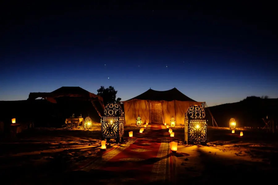A lantern-lit Berber tent in the desert under a deep blue night sky