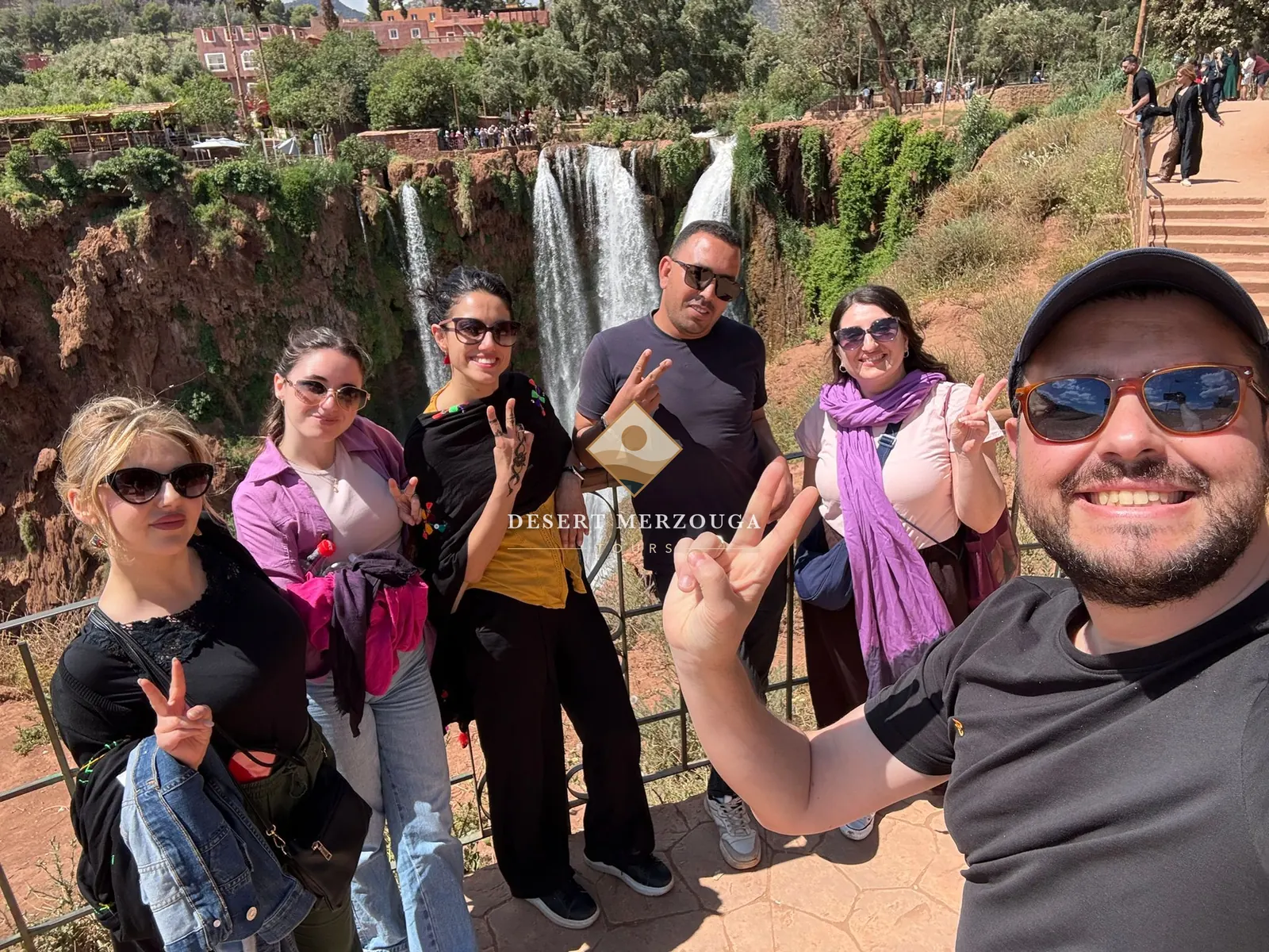 Smiling guests of Desert Merzouga Tours taking a group selfie at the Ouzoud waterfalls